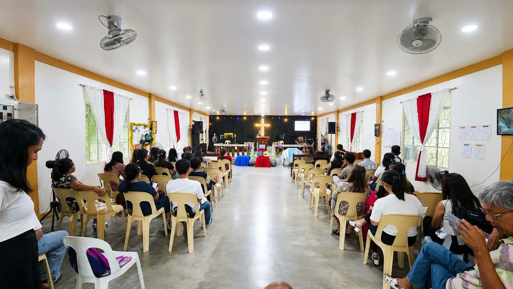 Wide view of the PCVCCI congregation seated in rows of chairs facing the stage with the illuminated cross