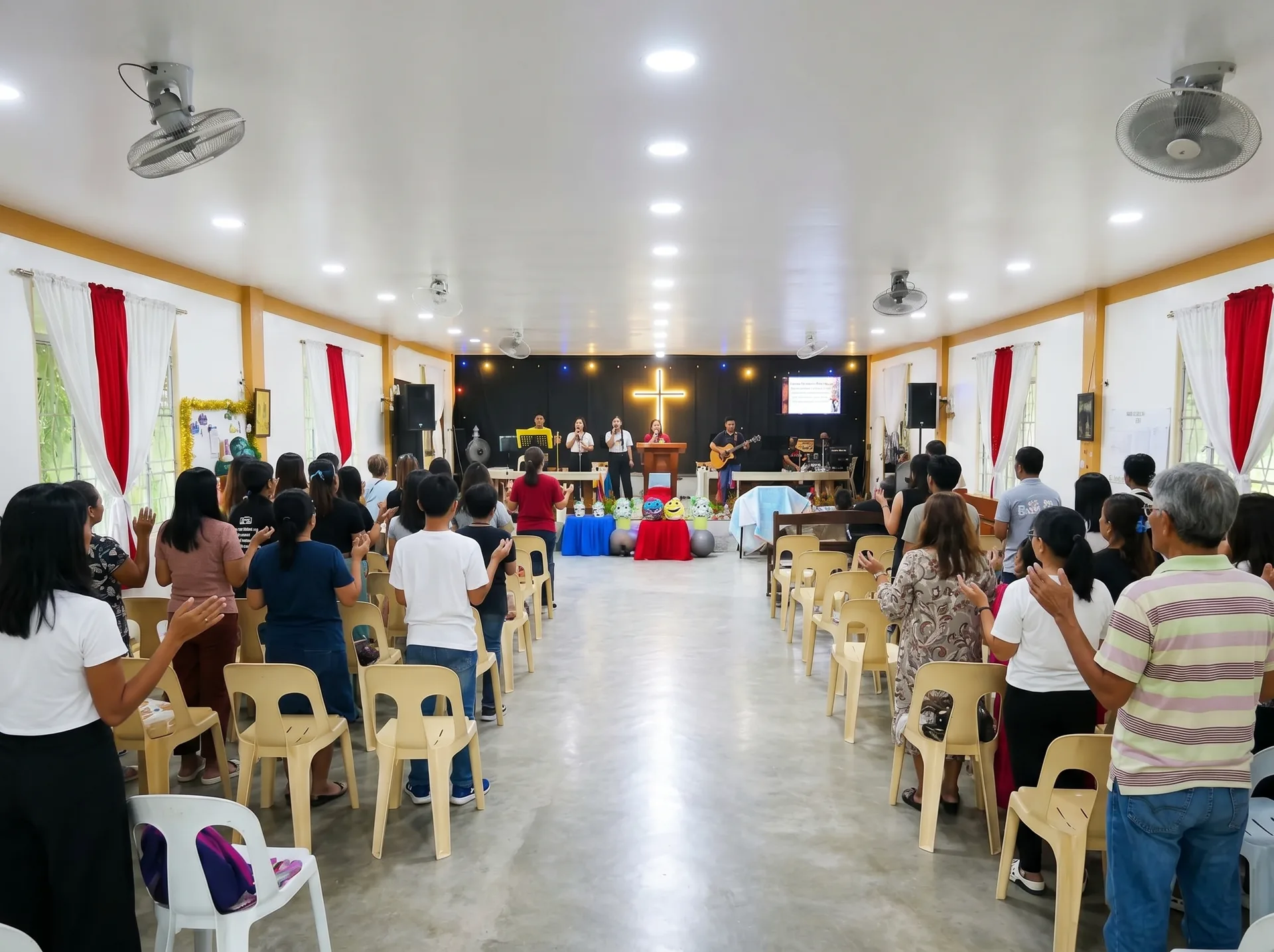 Congregation worshipping with hands raised as the praise team leads on the PCVCCI stage beneath the glowing cross